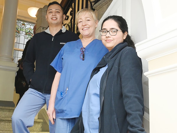 Three nurses standing on stairs looking down at camera